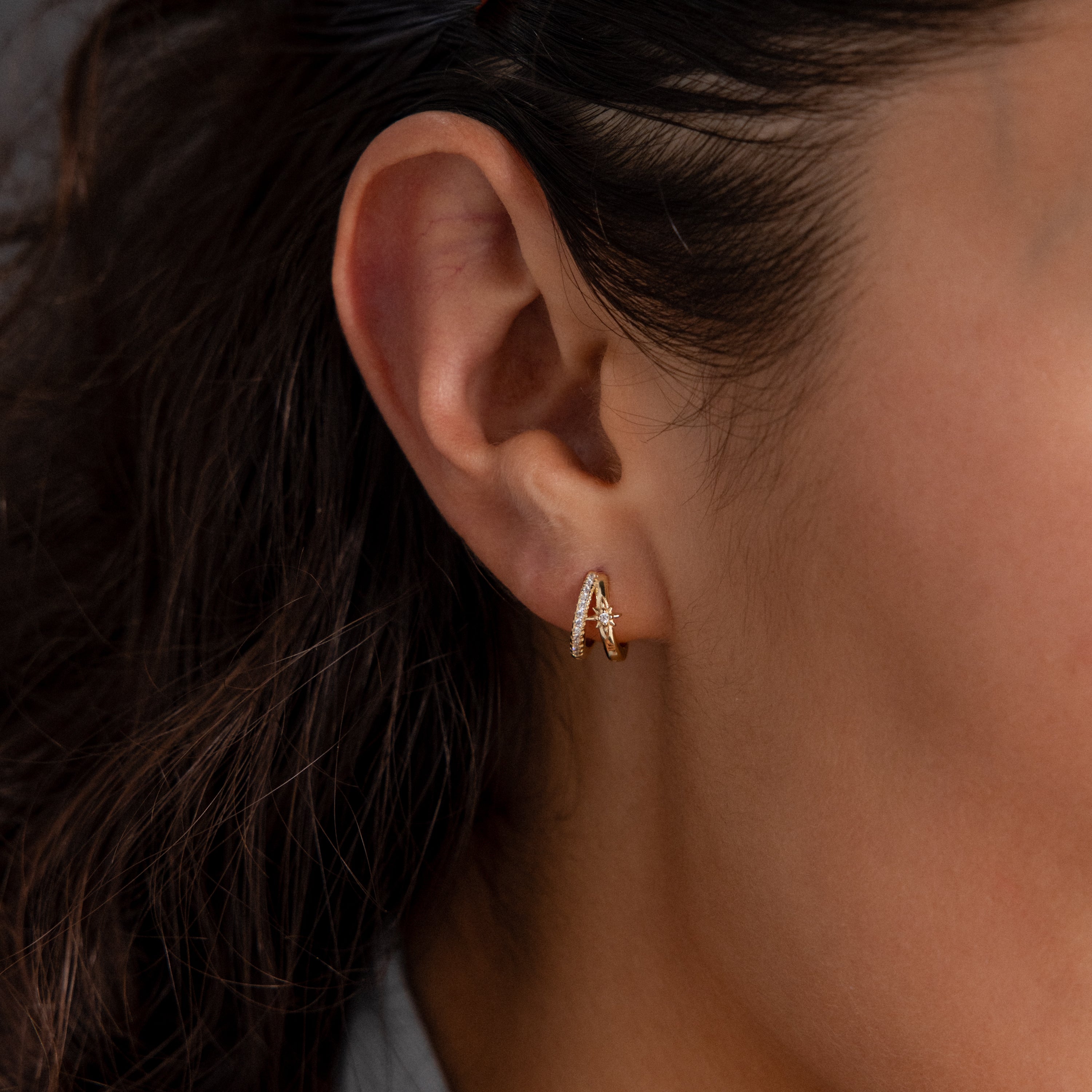 Close-up of a woman's ear wearing the Starburst Pave Duo Huggies in 18K Gold, featuring a decorative design.