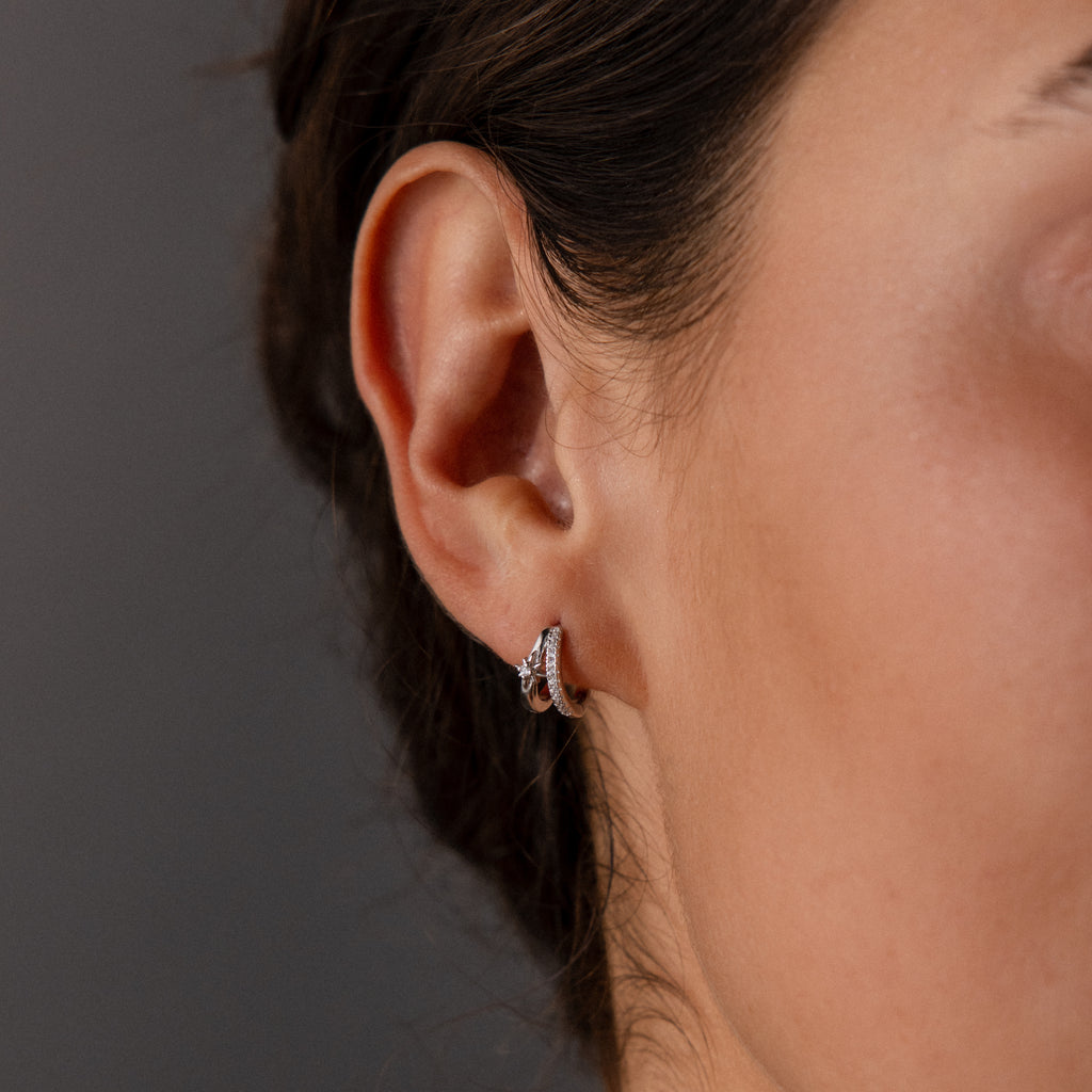 Close-up of a woman's ear wearing the Starburst Pave Duo Huggies in Sterling Silver—small hoops with sparkling clear stones for subtle elegance.