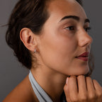 A woman with brown hair and light makeup wears the Starburst Pave Duo Huggies in Sterling Silver, looking thoughtful.