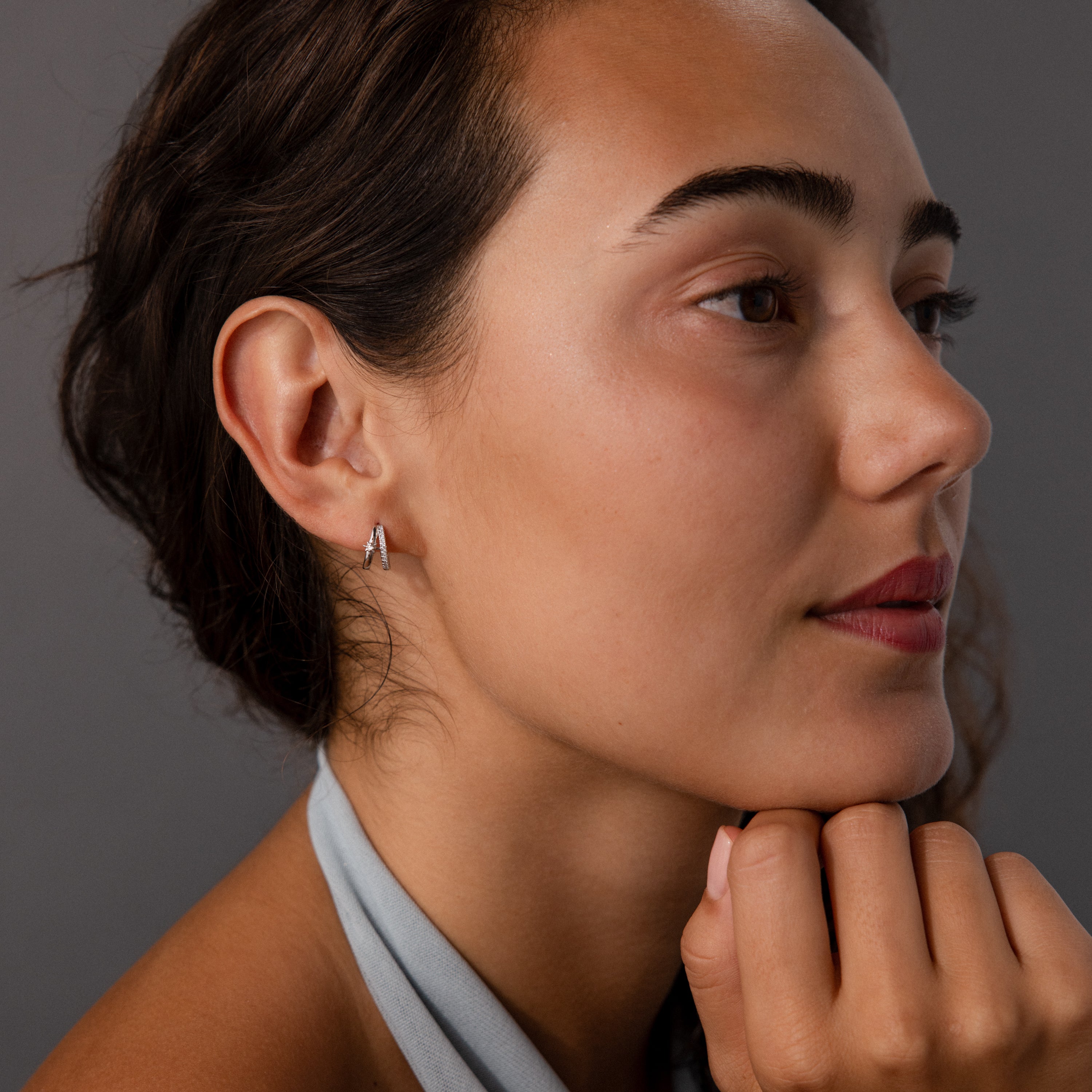 A woman with brown hair and light makeup wears the Starburst Pave Duo Huggies in Sterling Silver, looking thoughtful.
