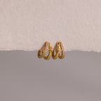 The Starburst Pave Duo Huggies feature two gold hoops—one with sparkling crystals, the other with a star charm—beautifully displayed on textured paper.