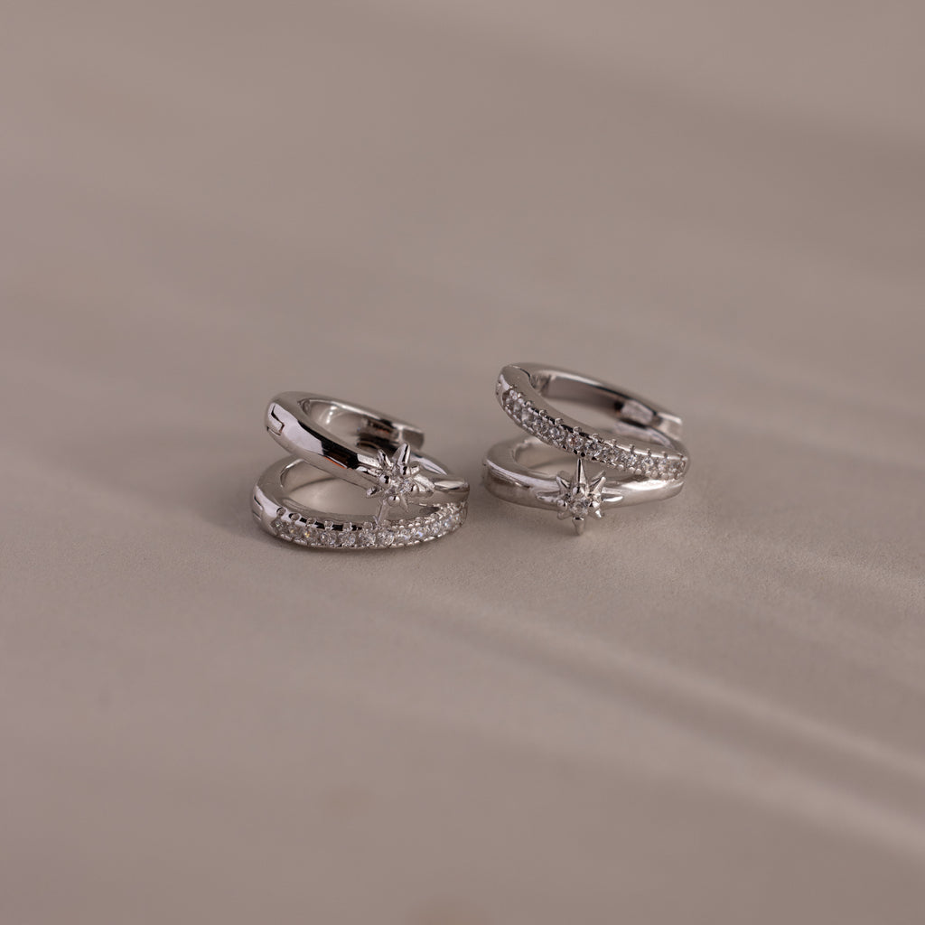 Two sterling silver rings with diamond accents and star motifs are displayed on a soft beige surface—perfect for pairing with the Starburst Pave Duo Huggies in Sterling Silver.
