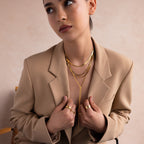 Woman in a tan blazer wearing a layered gold necklace, including the Long Y Herringbone Chain Necklace, looking off to the side.