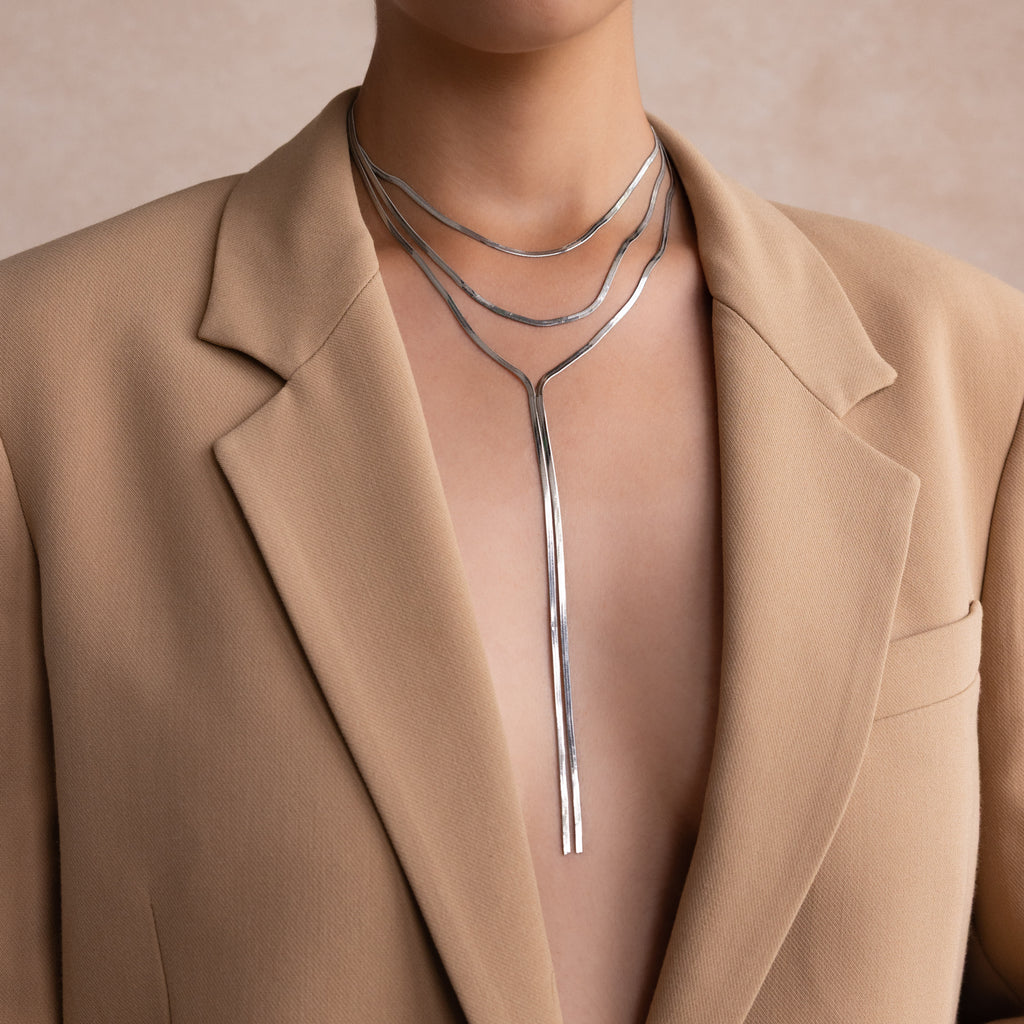 Person in a beige blazer wearing the Long Y Herringbone Chain Necklace in Silver, styled as a layered modern lariat with a sleek Y-shaped pendant.