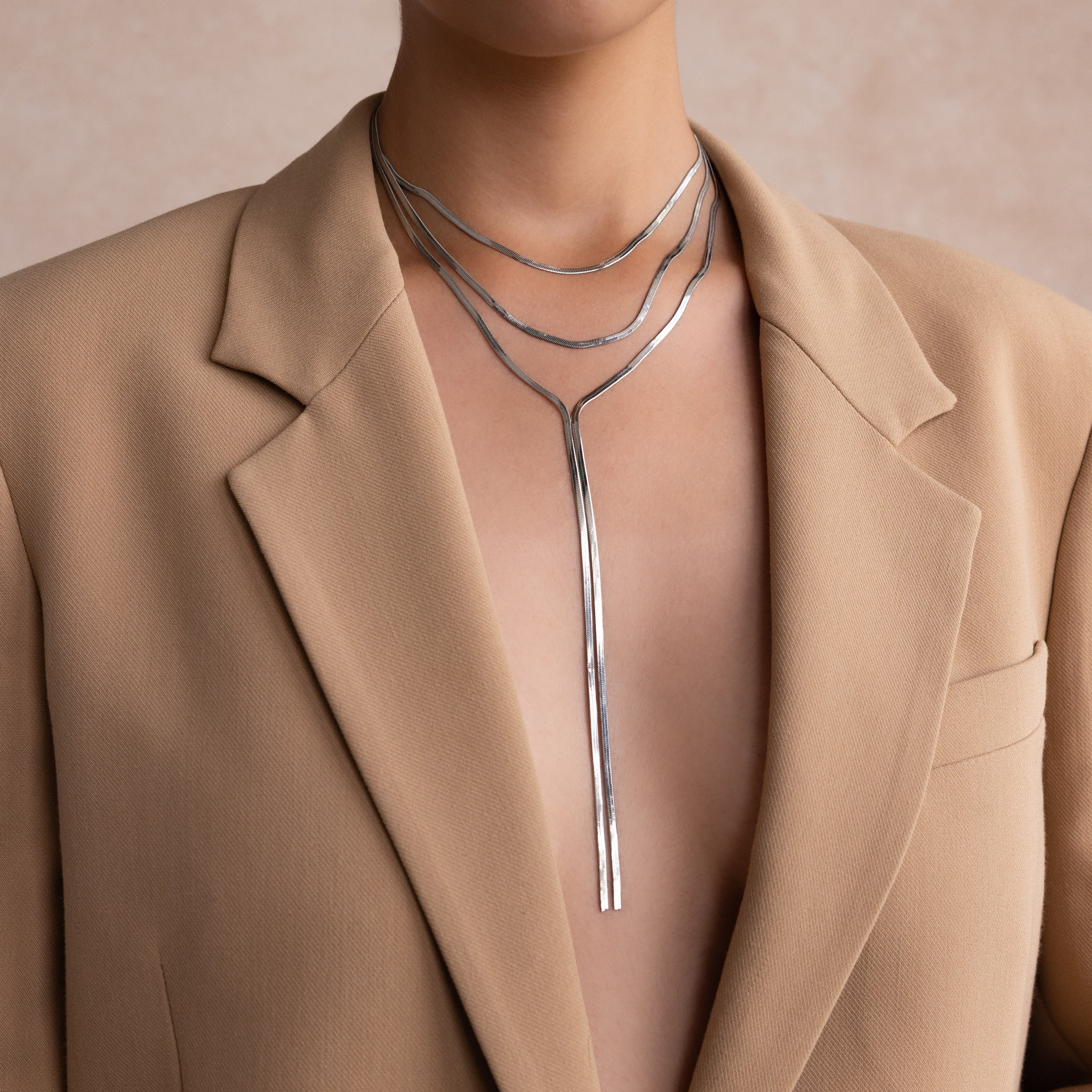 Person in a beige blazer wearing the Long Y Herringbone Chain Necklace in Silver, styled as a layered modern lariat with a sleek Y-shaped pendant.