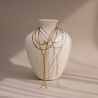 A white textured vase draped with thin gold and a Long Y Herringbone Chain Necklace in Silver, set against a neutral background.