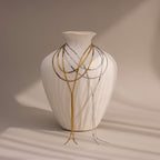 A white textured vase displays the Long Y Herringbone Chain Necklace, draped in layers of gold and silver against a neutral background.