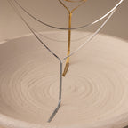 Thin metal wires shaped like trees stand in a textured sand-filled dish, mirroring the refined elegance of the Long Y Herringbone Chain Necklace in Silver.