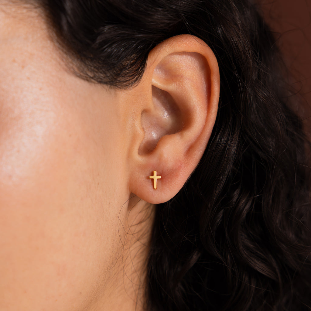 Close-up of model wearing dainty gold cross stud earrings.