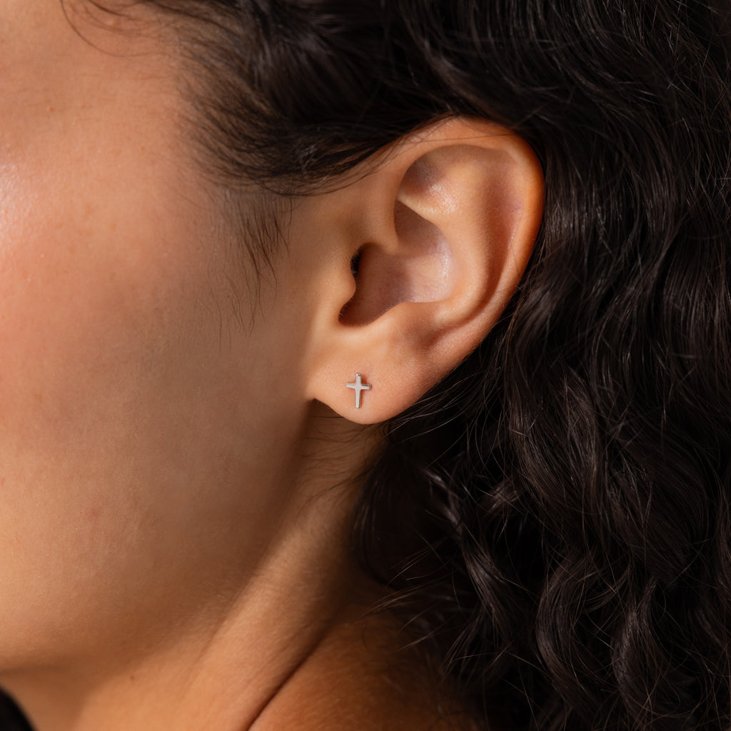 Model wearing dainty silver cross stud earrings.