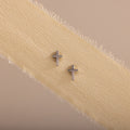 Dainty silver cross stud earrings displayed on a neutral ribbon fabric.