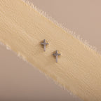 Dainty silver cross stud earrings displayed on a neutral ribbon fabric.