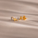 Pair of gold cross stud earrings with butterfly backings, displayed on a soft beige surface.