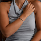 A woman in a sleeveless gray top showcases the Ribbed Diamond Bangle in White Gold with a polished finish on her wrist, her hand elegantly resting on her shoulder.