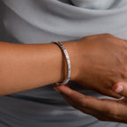 A hand wears the Ribbed Diamond Bangle in White Gold, featuring a polished finish, with a soft gray fabric background.