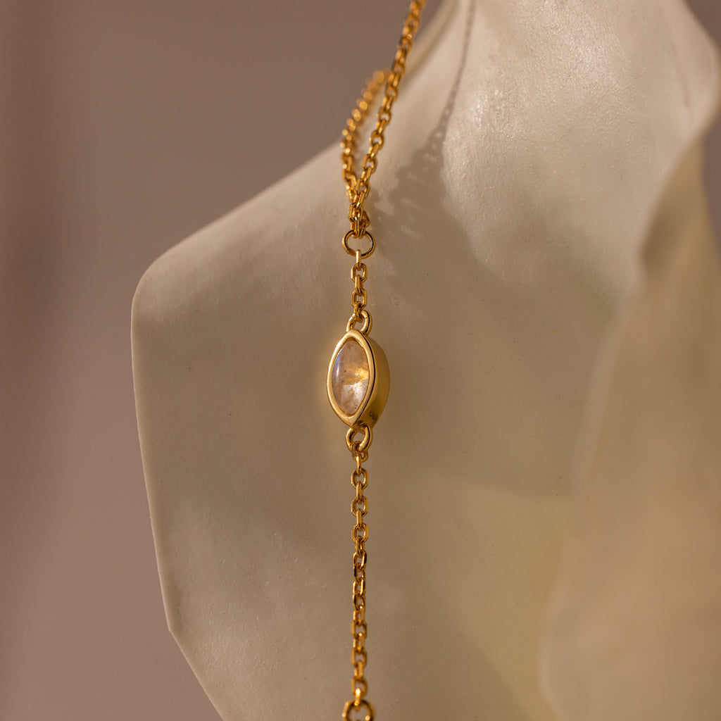 Moonstone Hand Chain Bracelet in 18K Gold featuring an oval moonstone charm, elegantly displayed against a sculpted white background—perfect for fans of celestial-inspired jewelry.