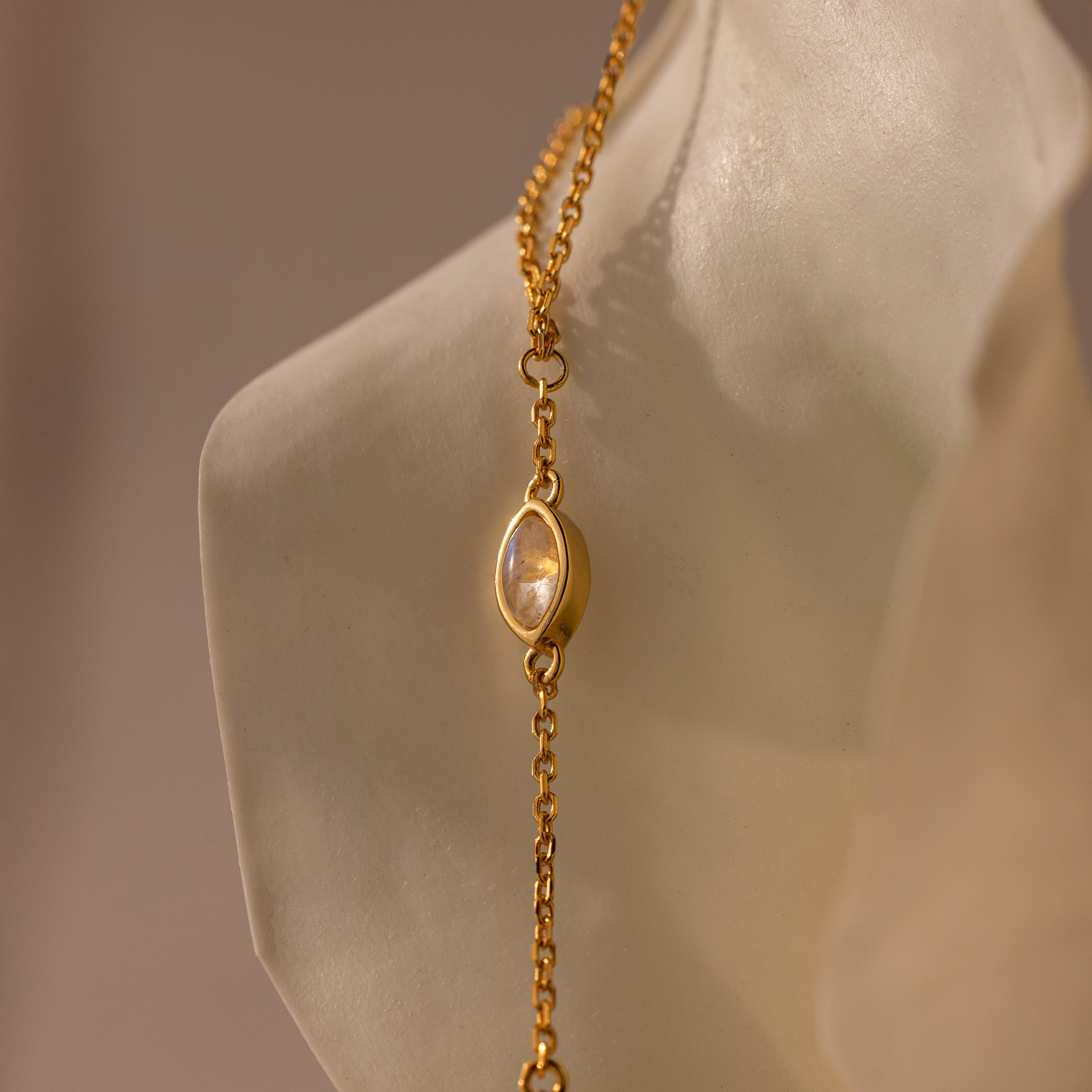 Moonstone Hand Chain Bracelet in 18K Gold featuring an oval moonstone charm, elegantly displayed against a sculpted white background—perfect for fans of celestial-inspired jewelry.