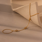 The Moonstone Hand Chain Bracelet in 18K Gold features delicate oval accents and is displayed on a curved, textured beige surface—an elegant celestial-inspired jewelry piece.