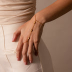 A woman's hand adorned with the Moonstone Hand Chain Bracelet in 18K Gold rests on her cream-colored pants, highlighting the subtle elegance of this celestial-inspired jewelry.