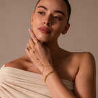A woman with bare shoulders wears gold celestial jewelry—a Moonstone Hand Chain Bracelet in 18K Gold—along with rings and a chain, set against a neutral background.