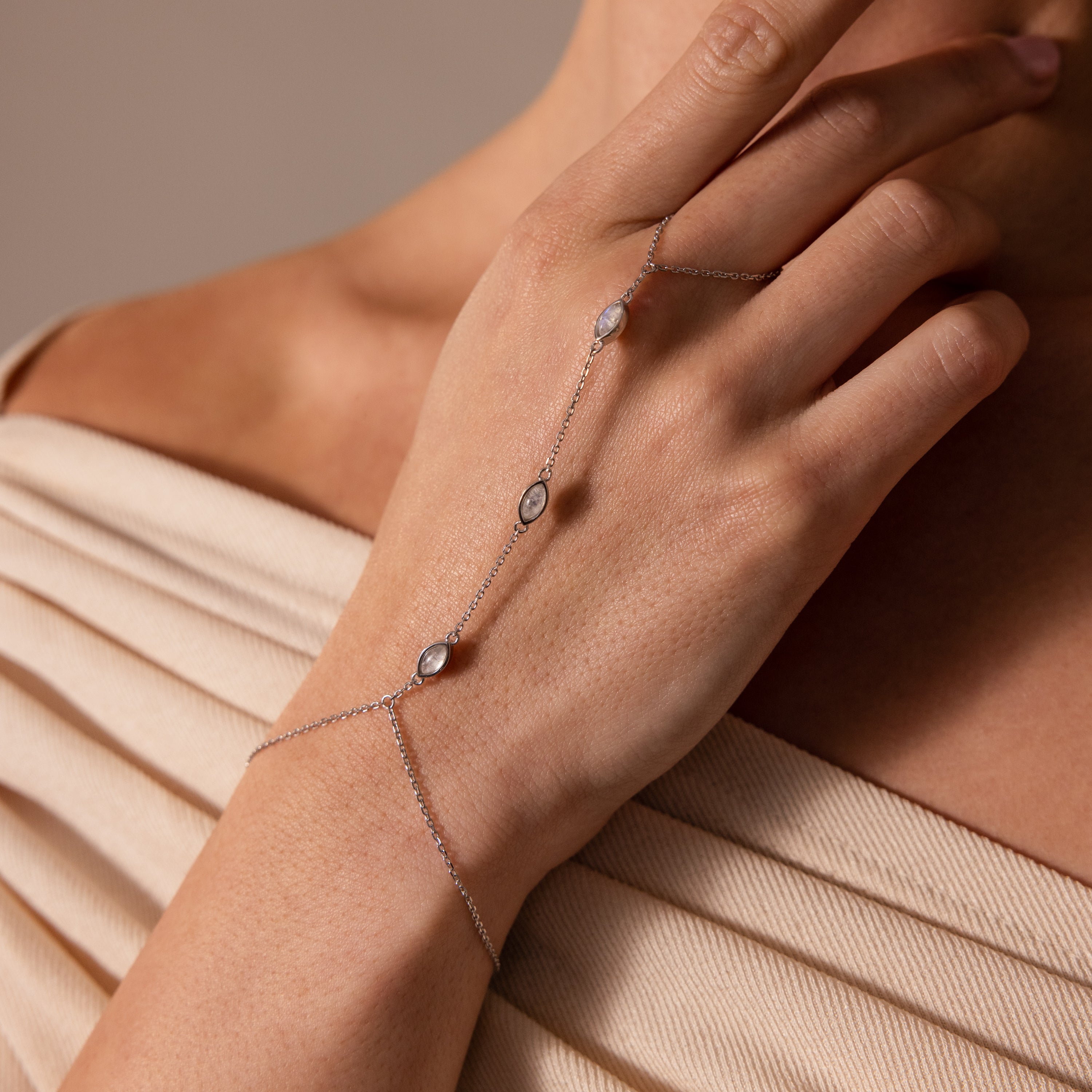 A hand wearing the Moonstone Hand Chain Bracelet in Silver, adorned with three small moonstones, is held near the collarbone—an elegant and celestial jewelry piece.