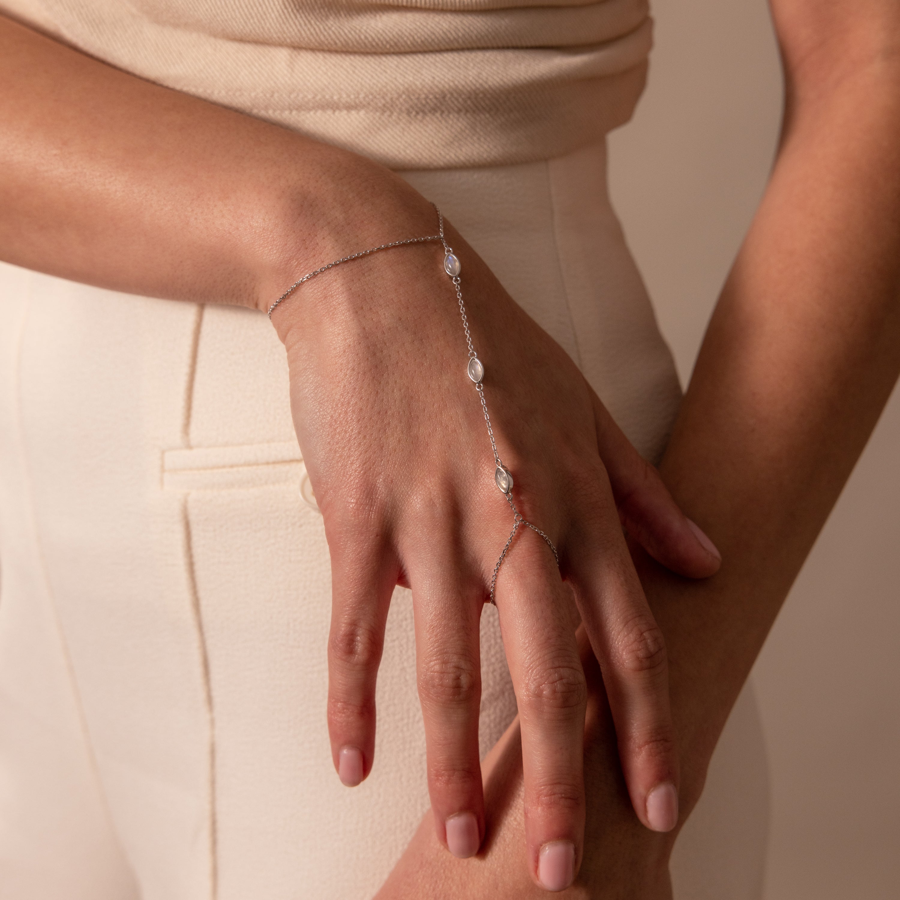 The Moonstone Hand Chain Bracelet in Silver adds elegance to any woman's look, perfectly complementing her beige pants and top.