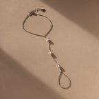 The Moonstone Hand Chain Bracelet in Silver features three oval gemstones and is shown on a beige background with gentle shadows.