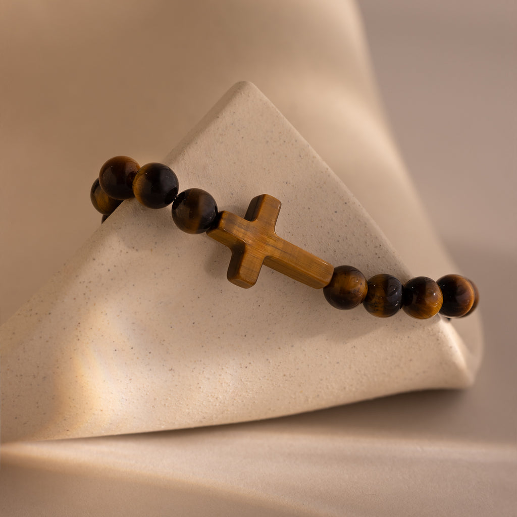 Close-up of the Tigers Eye Cross Bracelet featuring round polished tiger's eye beads and a horizontal tiger's eye cross charm, displayed on a neutral stone surface.