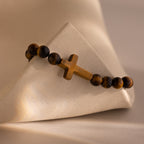 Close-up of the Tigers Eye Cross Bracelet featuring round polished tiger's eye beads and a horizontal tiger's eye cross charm, displayed on a neutral stone surface.
