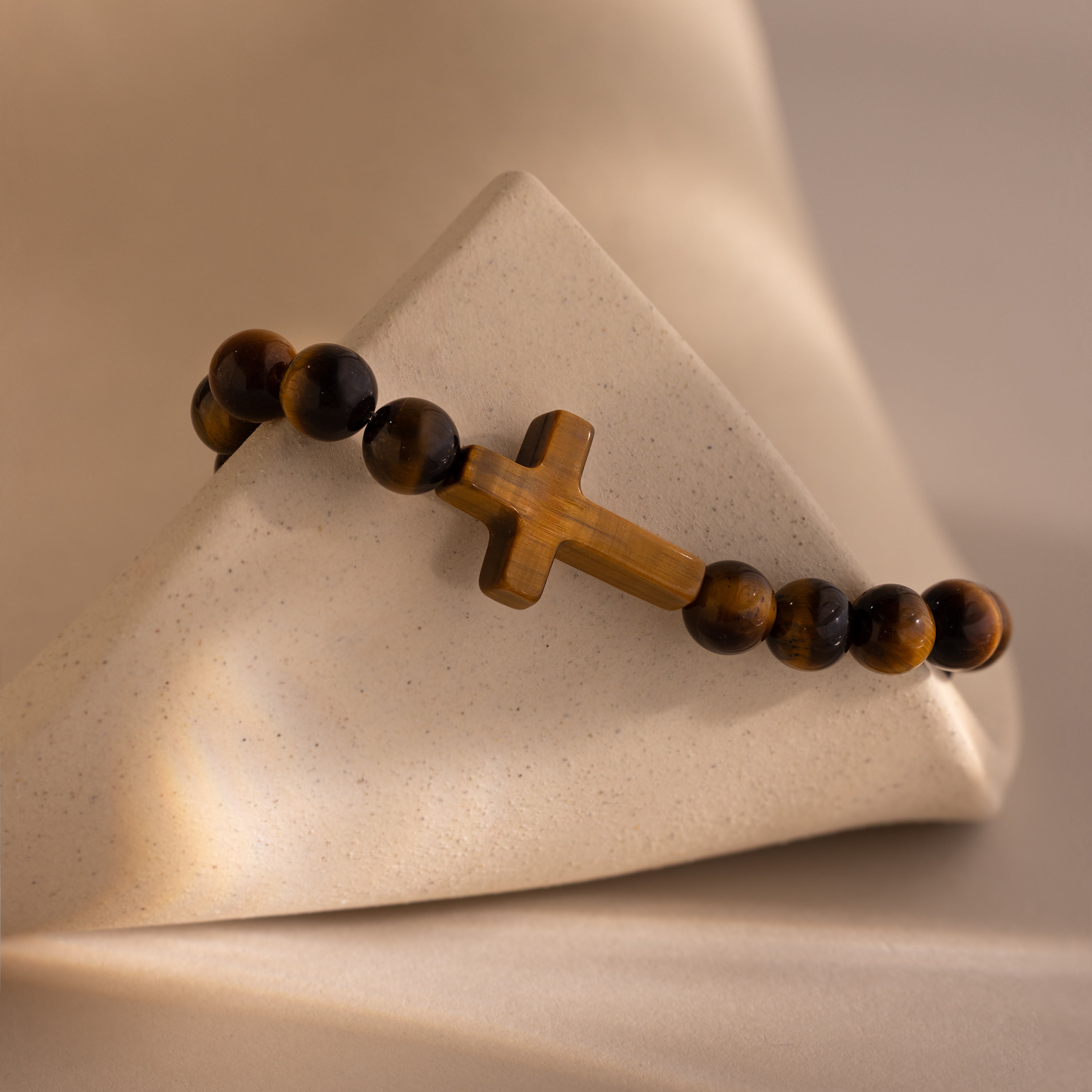 Close-up of the Tigers Eye Cross Bracelet featuring round polished tiger's eye beads and a horizontal tiger's eye cross charm, displayed on a neutral stone surface.