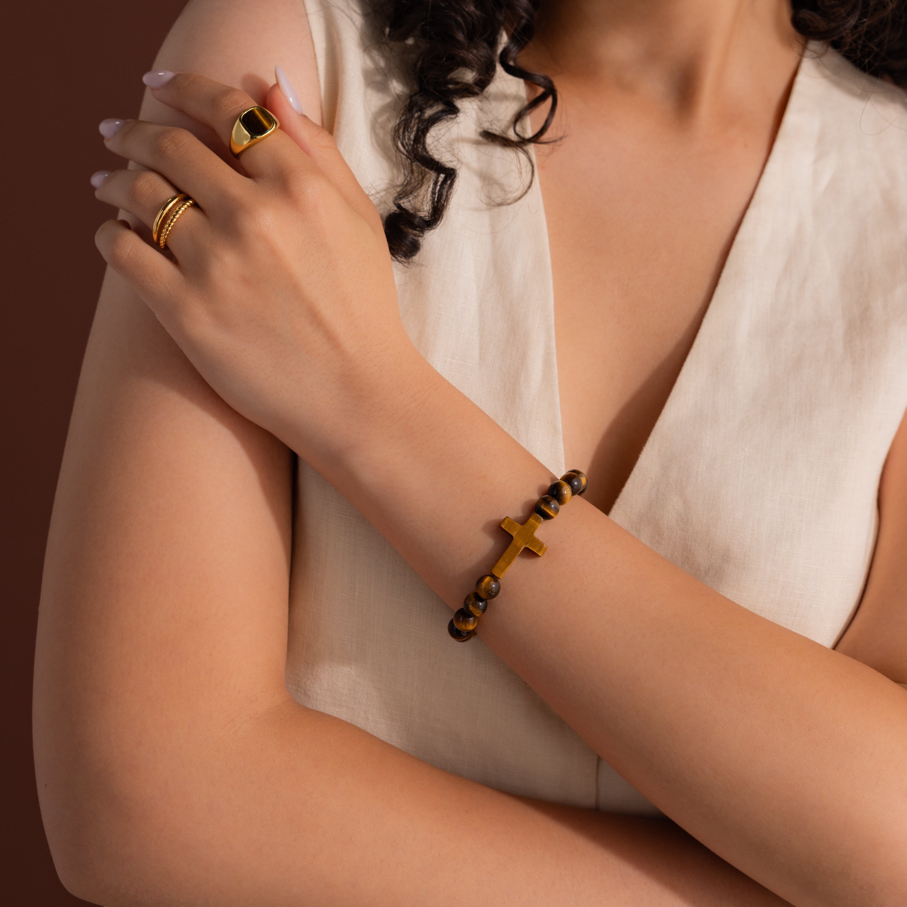 Model wearing the Tigers Eye Cross Bracelet, styled with a gold tigers eye signet ring and gold duo band ring.