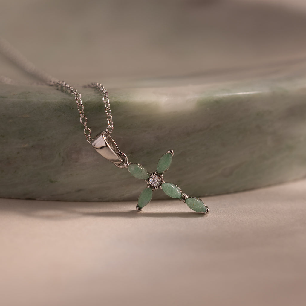 Silver chain necklace featuring a marquise jade stone cross pendant with a sparkling CZ diamond, displayed on a soft green stone surface.