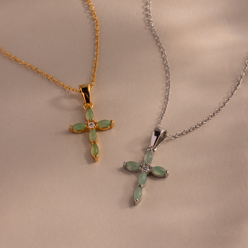 Flat-lay of a two jade cross pendant necklaces in gold and silver, each featuring marquise-cut green stones and a CZ diamond center.