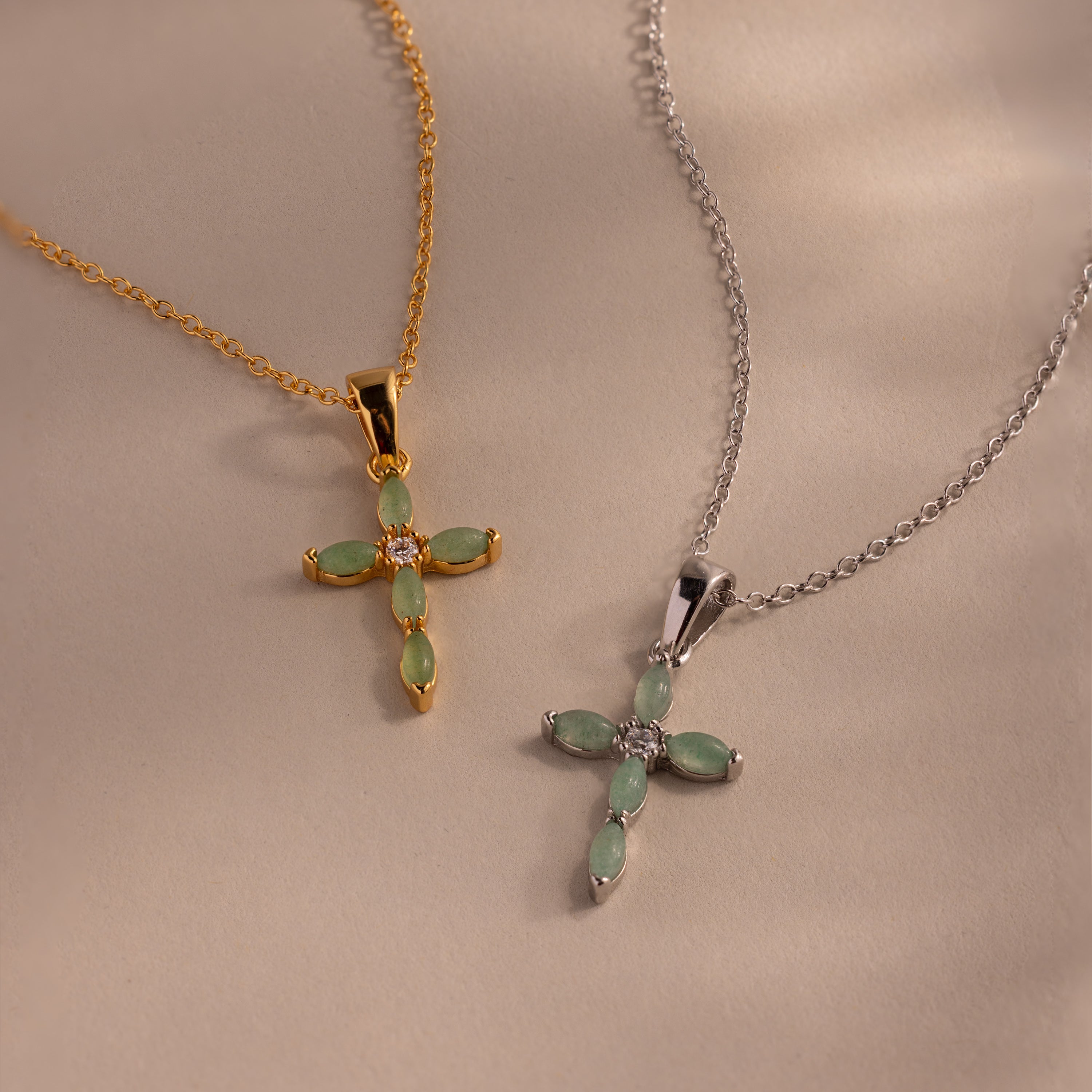 Flat-lay of a two jade cross pendant necklaces in gold and silver, each featuring marquise-cut green stones and a CZ diamond center.