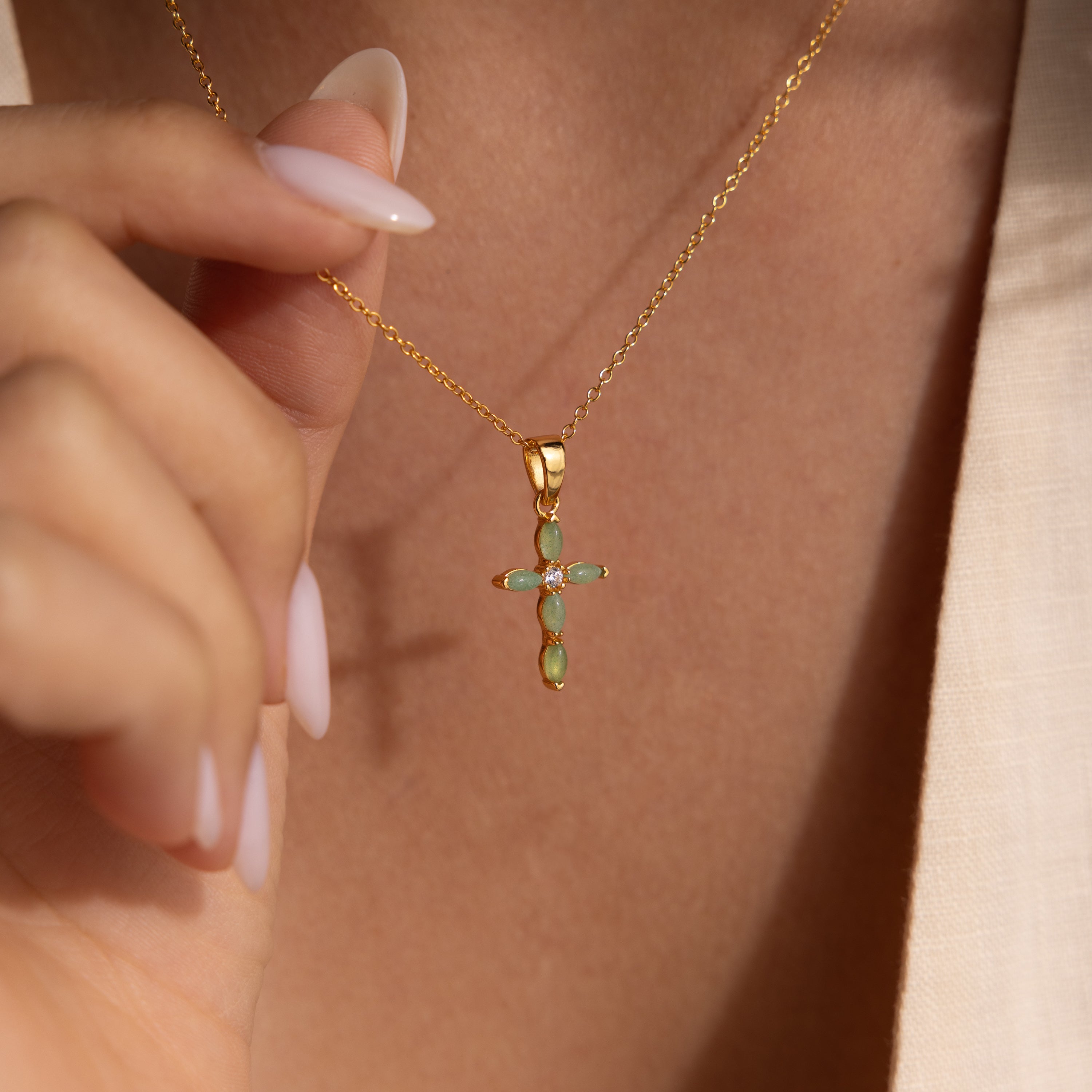 Close-up of model wearing a gold necklace with a jade cross pendant, featuring marquise-cut green stones and a CZ diamond center.