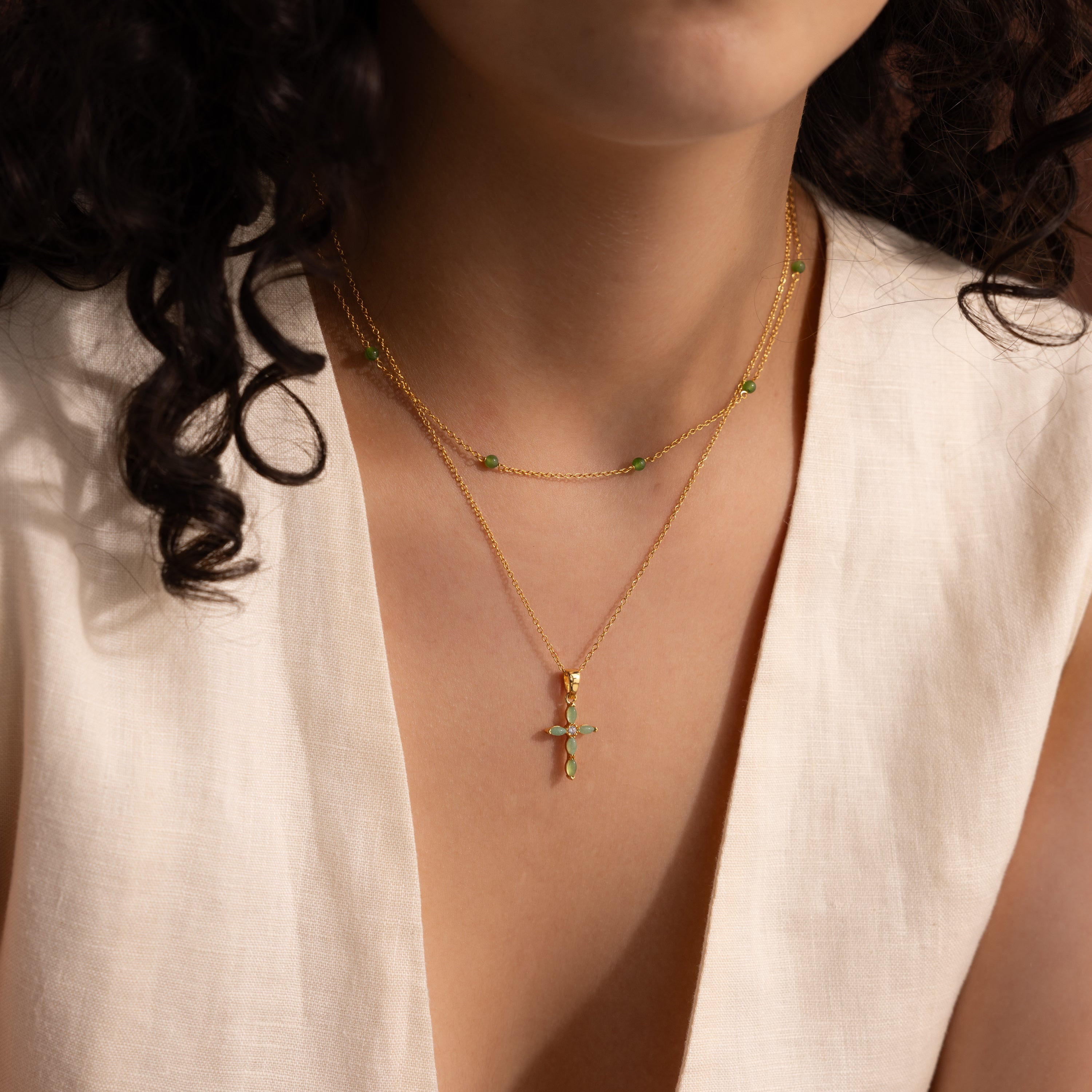 Model wearing a dainty gold jade cross pendant necklace layered with a gold jade station choker necklace.