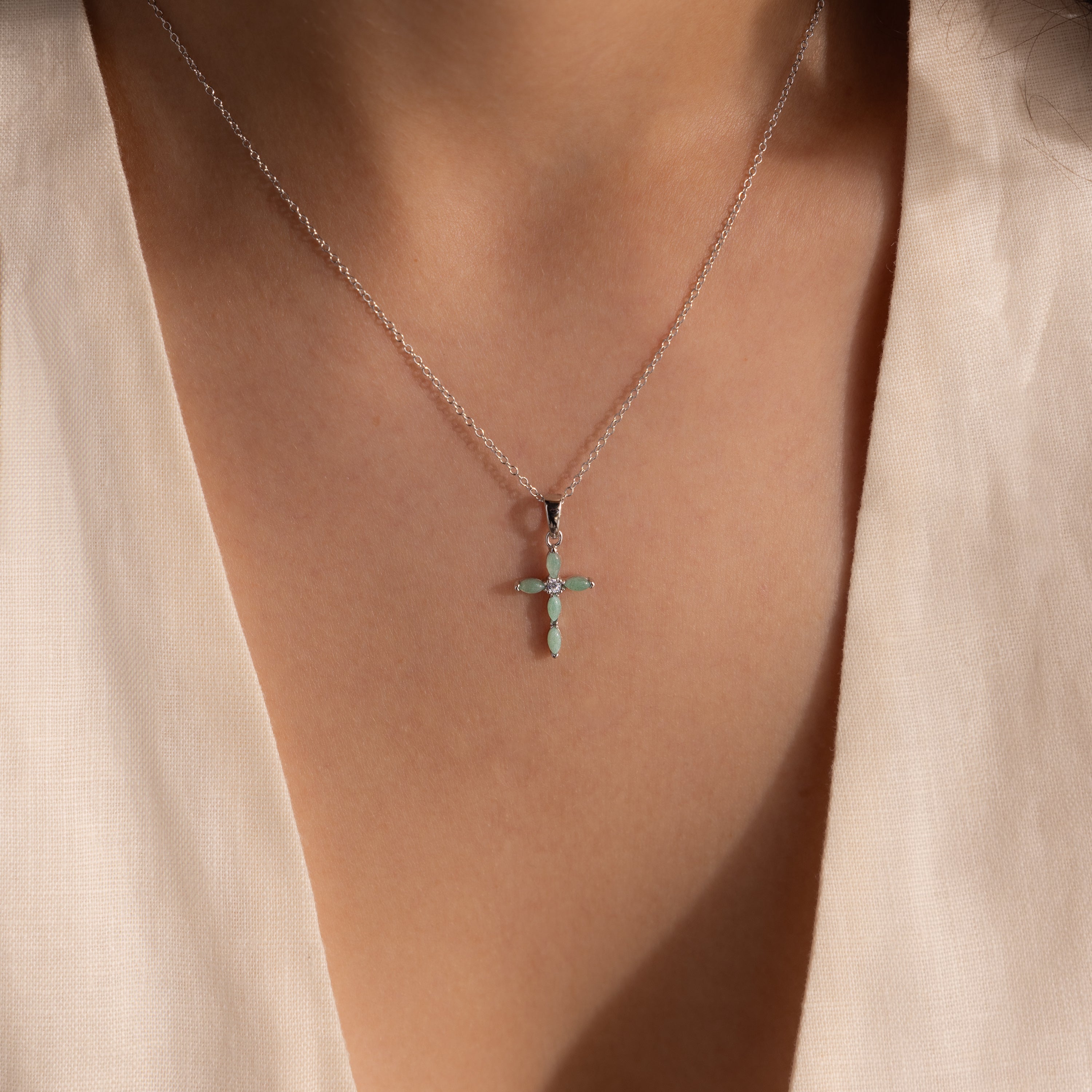 Model wearing a silver necklace with a jade cross pendant, featuring marquise-cut green stones and a CZ diamond center.