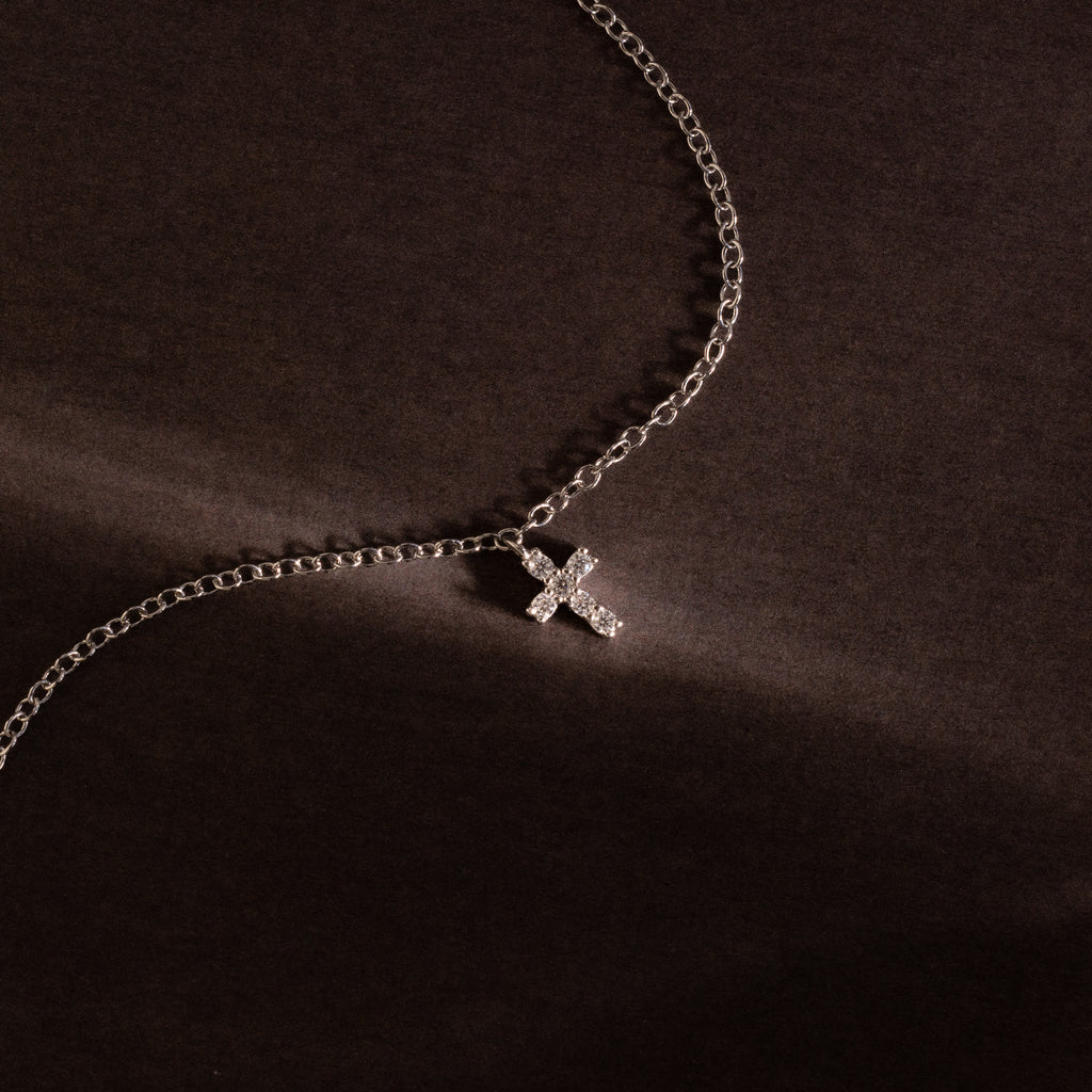 Silver chain bracelet featuring a sparkling crystal cross charm, photographed against a dark textured background for a bold and elegant presentation.