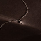 Silver chain bracelet featuring a sparkling crystal cross charm, photographed against a dark textured background for a bold and elegant presentation.