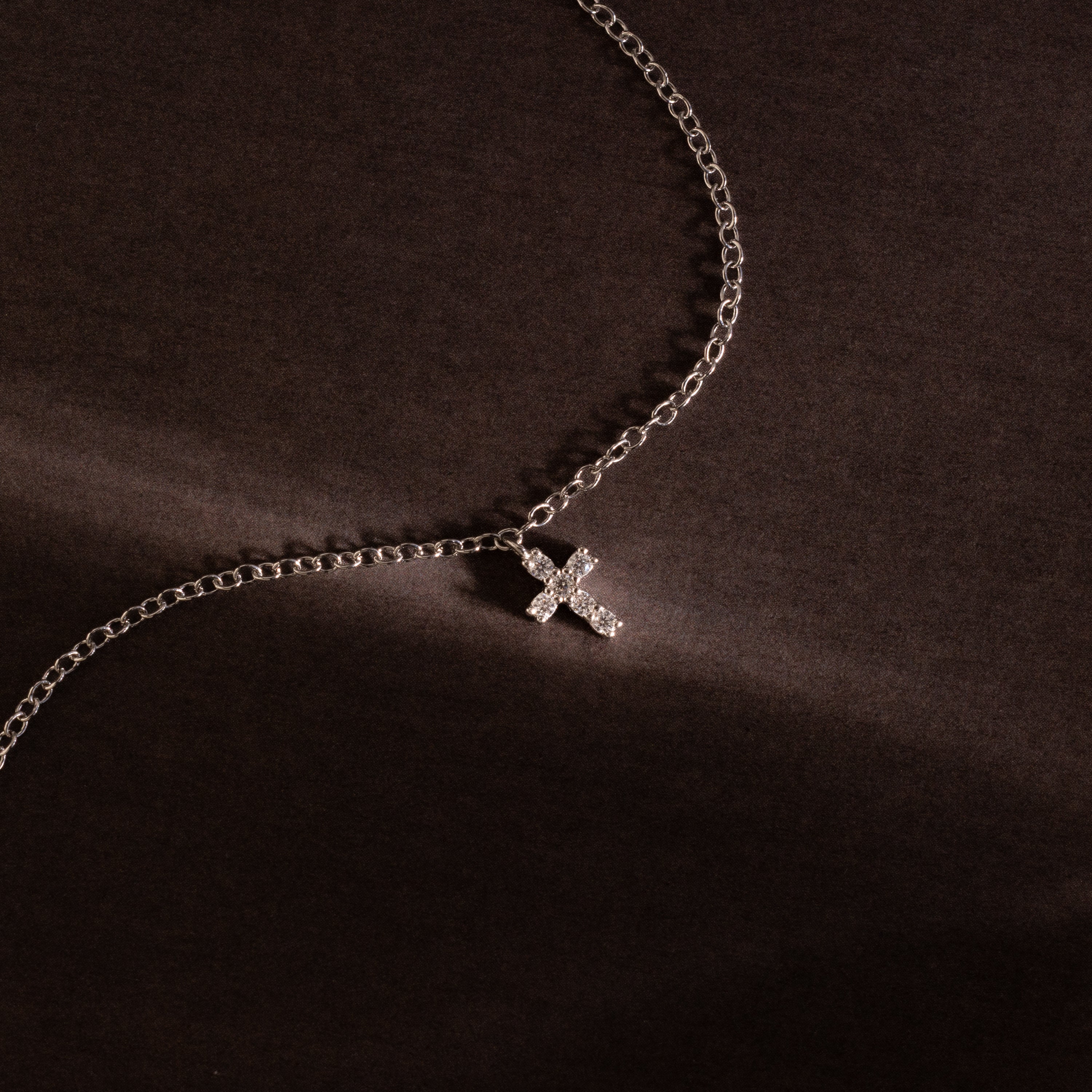 Silver chain bracelet featuring a sparkling crystal cross charm, photographed against a dark textured background for a bold and elegant presentation.