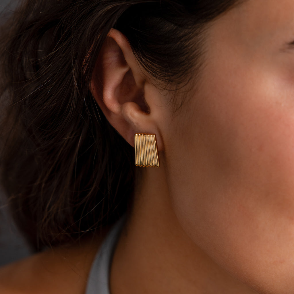 Close-up of a woman's ear wearing Ribbed Earrings—rectangular, gold, and textured—for an elegant touch of contemporary jewelry style.
