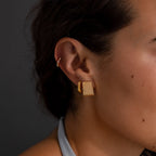 Close-up of a woman's ear wearing Ribbed Earrings in 18K Gold with a textured column design, set against a dark background.