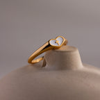 Close-up of a gold heart-shaped ring with a white enamel face and small gold cross.