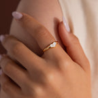 Close-up of model wearing a gold heart-shaped ring with white enamel face and small gold cross.