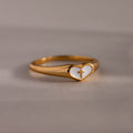 Close-up of a gold heart-shaped ring with white enamel face and small gold cross, displayed on a neutral surface.