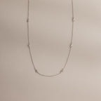 The Dainty Bow Necklace laid flat on a neutral surface, showing its full length, silver chain, and petite bow details.