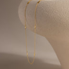 Delicate gold Bow Station Necklace draped over a curved neutral-toned surface.