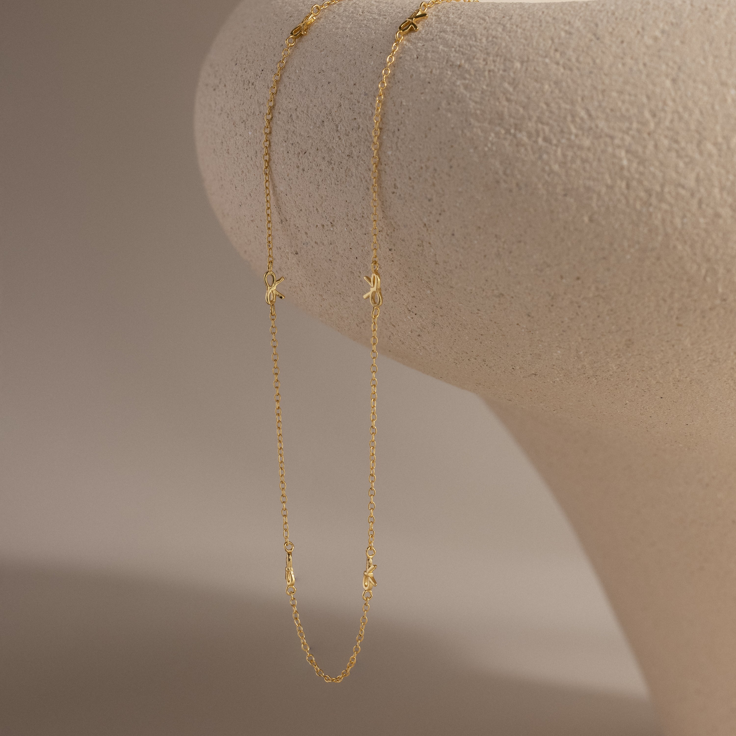 Delicate gold Bow Station Necklace draped over a curved neutral-toned surface.