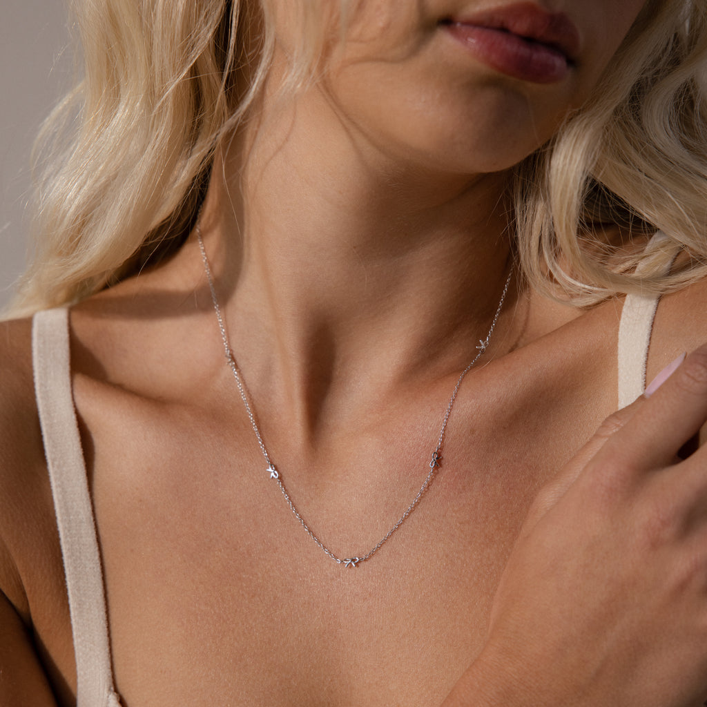 A woman wearing the silver Dainty Bow Necklace, which rests lightly along her collarbone.