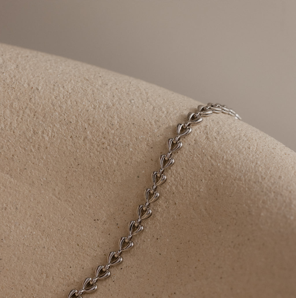 Silver Tiny Link Heart Bracelet draped over a textured ceramic prop.